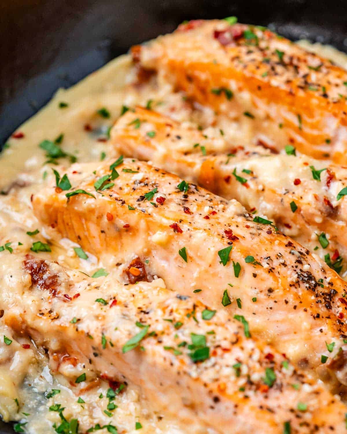 Seared salmon filets in a creamy sauce in a black skillet.