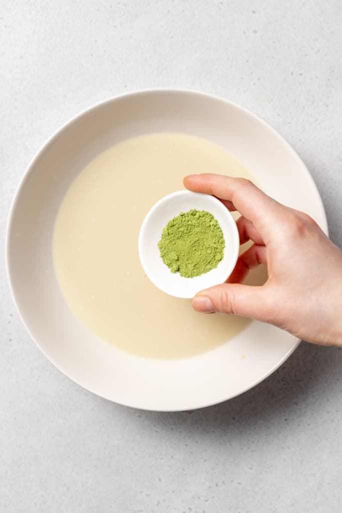 hand pouring matcha powder over milk