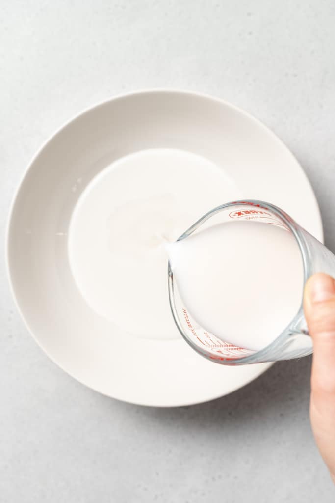 hand pouring milk in jar over a bowl