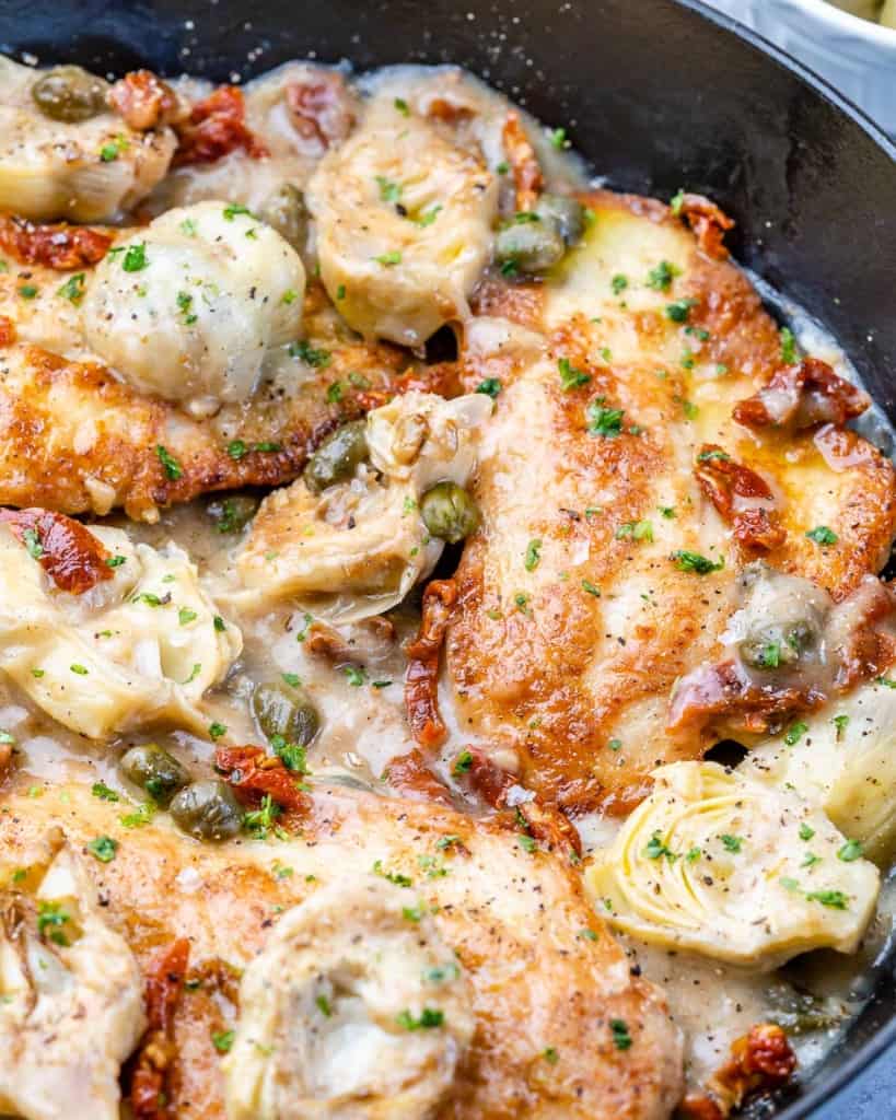 close up view of seared chicken in a black skillet with capers lemon sauce 