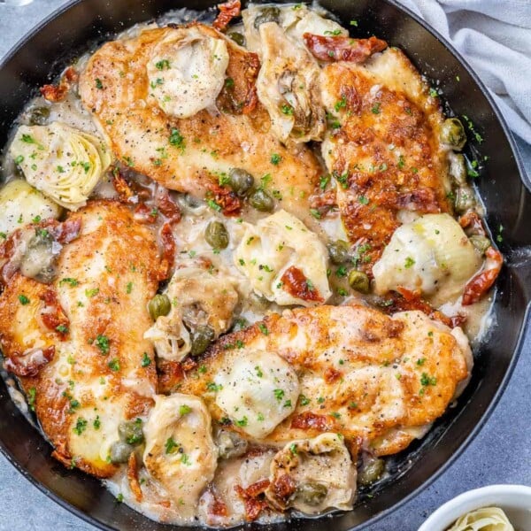 Mediterranean Chicken in a black skillet with artichokes.