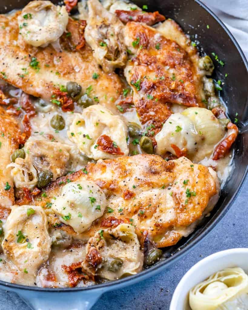 side shot of chicken breast in a Mediterranean lemon sauce in black skillet 