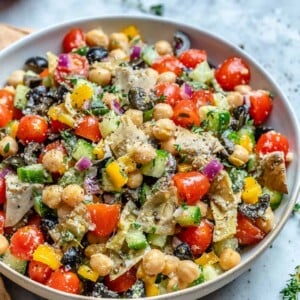 vegetarian chickpea salad recipe in a round bowl with olives, tomatoes, and artichokes.
