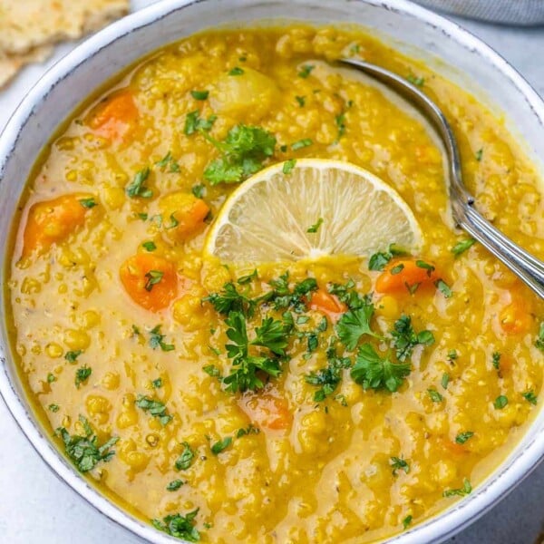 top view lentil soup in white bowl with spoon in it and lemon slice garnish