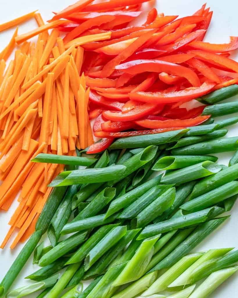 sliced peppers, carrots, and green onions on a cutting board