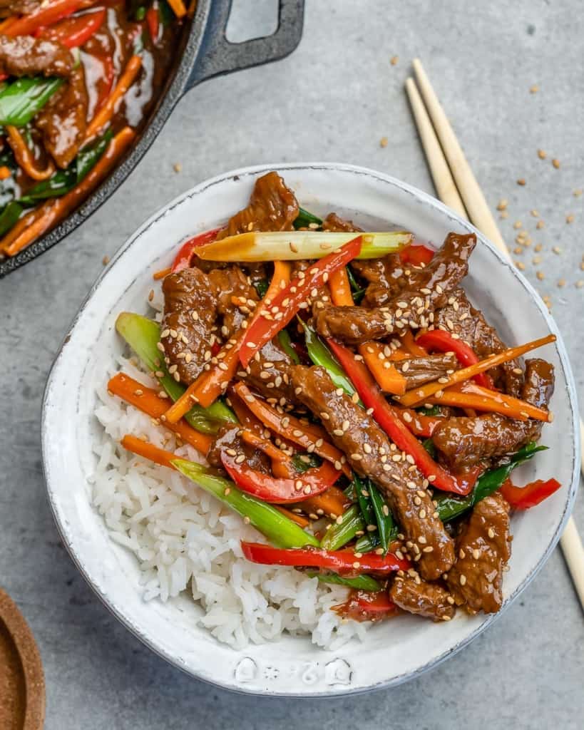 chop sticks next to a bowl of beef stir fry in a white bowl with rice