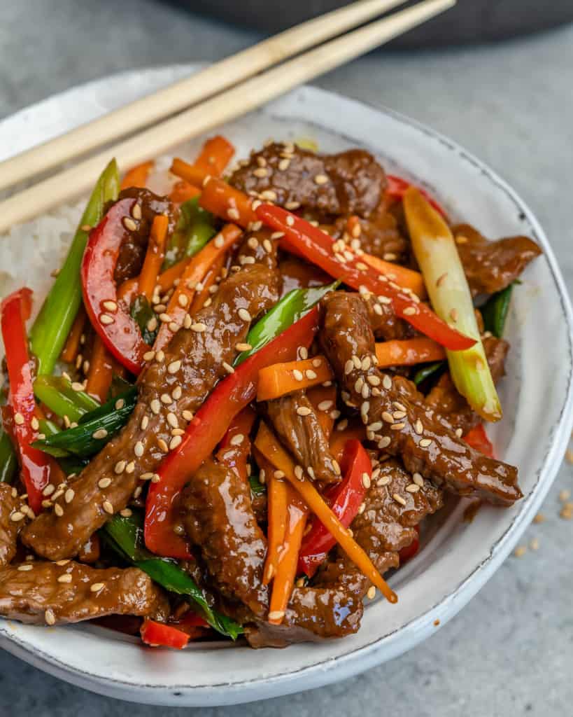 side view of mongolian beef in a white bowl with chop sticks