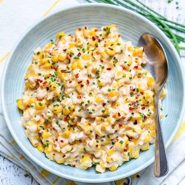 top view of a round plate with cheesy corn topped with chili flakes and chives with spoon in plate on the right side
