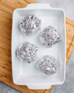 4 covered onions with foil in a baking dish.