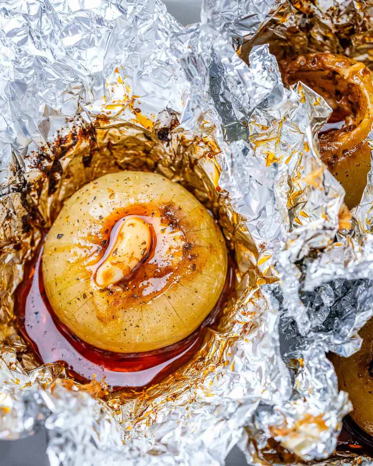 Baked onion with seasonings and butter in a foil wrap, opened, on a cutting board.