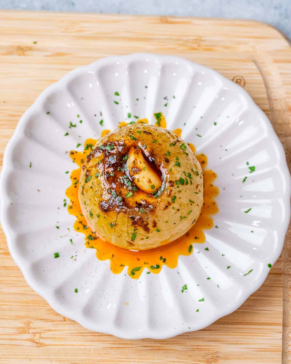 Baked onion boil with seasoned melted butter on a round white plate.