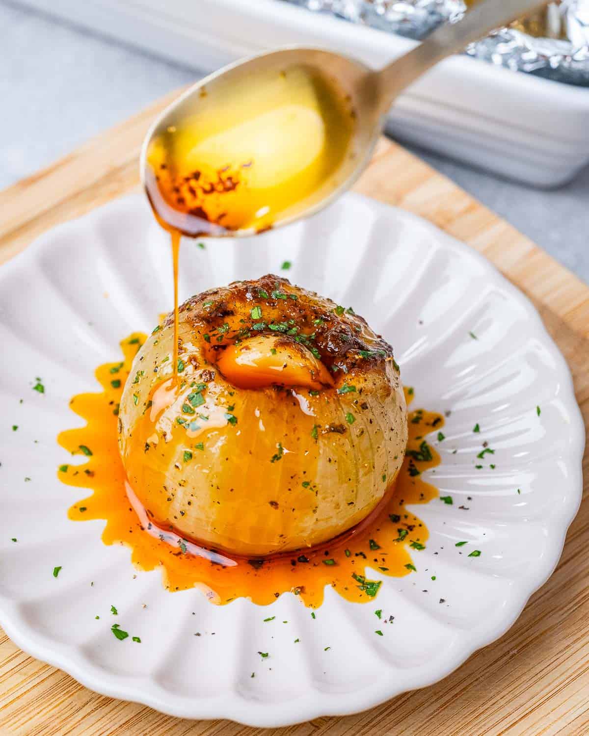 Spoon drizzling seasoned oil over cooked onion on a plate.