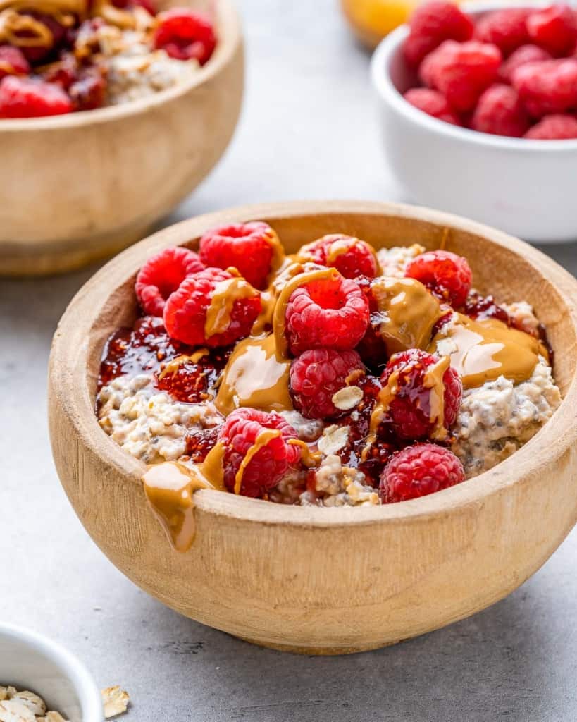 side shot of overnight oatmeal in a tan wood bowl topped with berries and peanut butter 