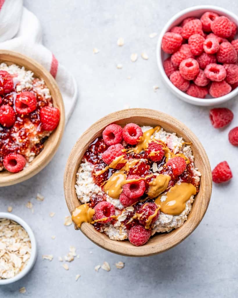 top view of two bowls of overnight oatmeal topped with raspberry and peanut butter with a side bowl top right of raspberries