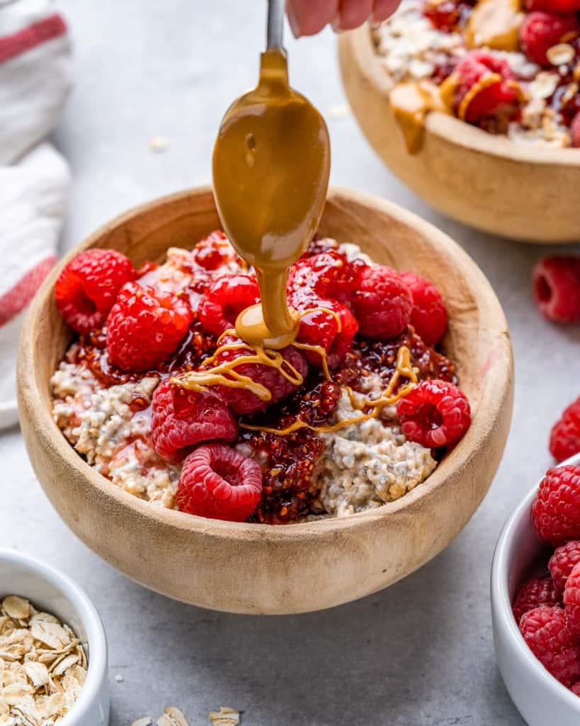 spoon drizzling peanut butter over a bowl of oatmeal topped with berries 