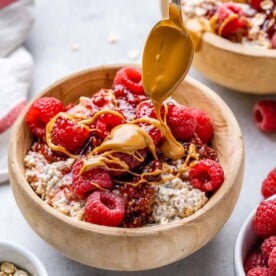 overnight oats in a brown wooden bowl topped with peanut butter drizzle and raspberries.