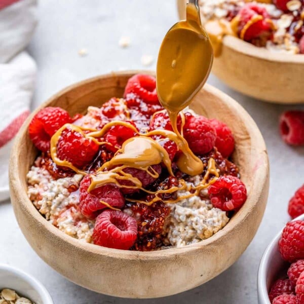 overnight oats in a brown wooden bowl topped with peanut butter drizzle and raspberries.