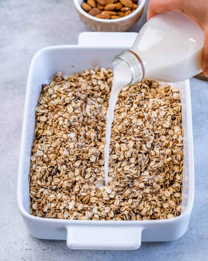 Pouring milk over oat mixture in a white casserole dish.