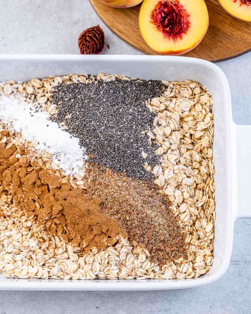 Mixing oats with spices and chia seeds in a white baking dish.
