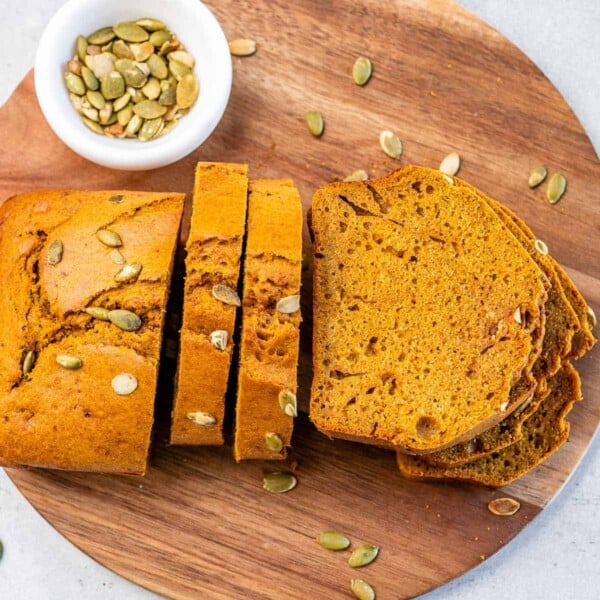 wooden platter with pumpkin bread slices. with a small cup of pumpkin seeds on the side of it.