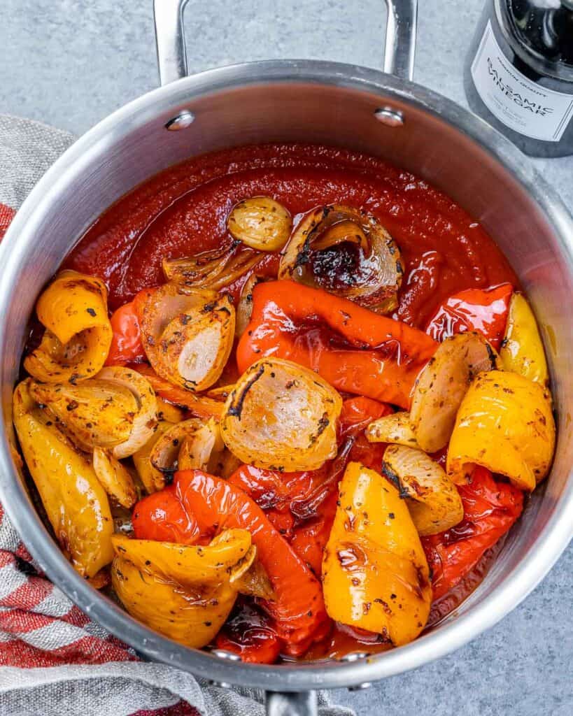 Adding roasted veggies to a pot with stock and tomato sauce.