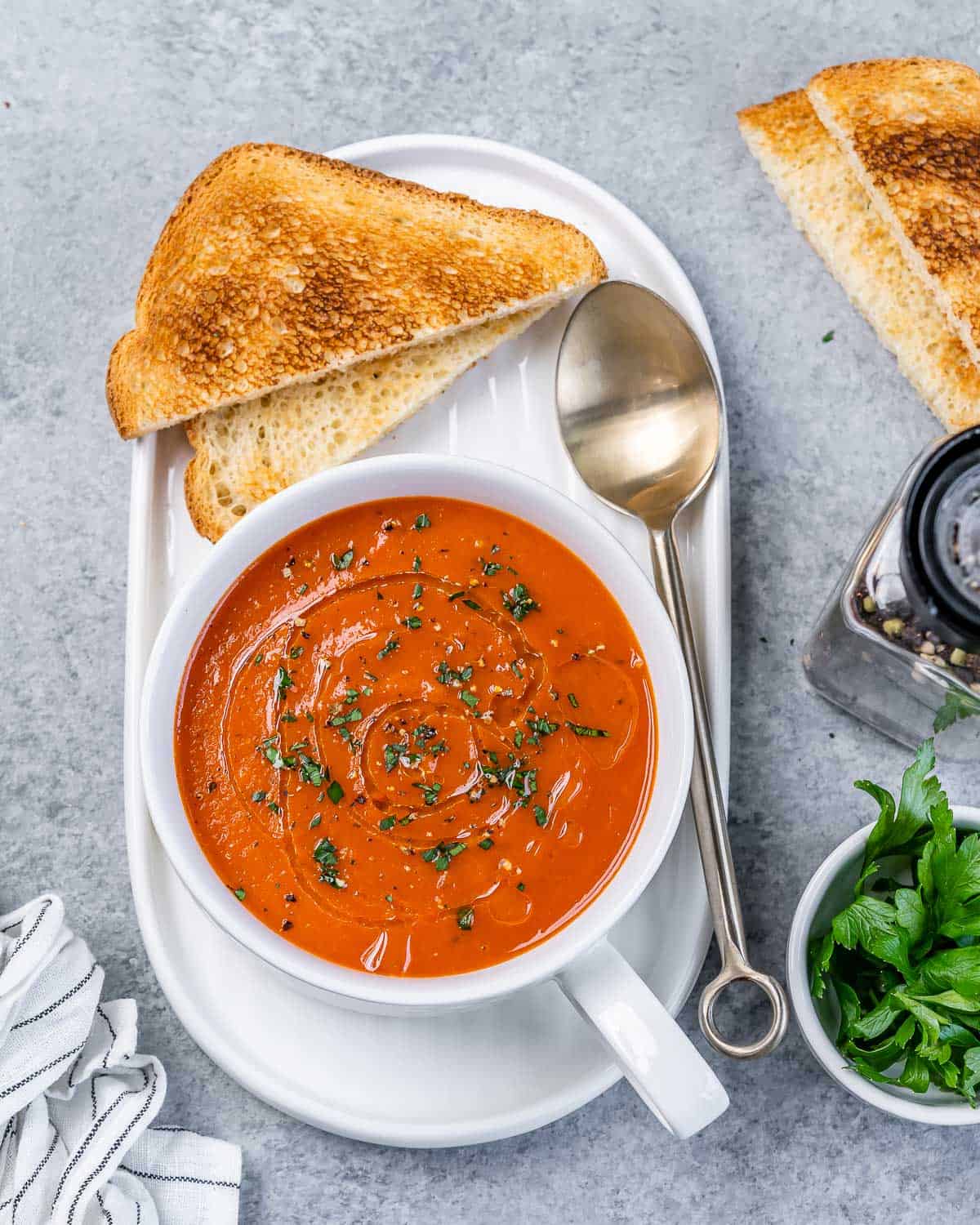 Top view of a small round white bowl of pepper soup on a plate with toast next to it.