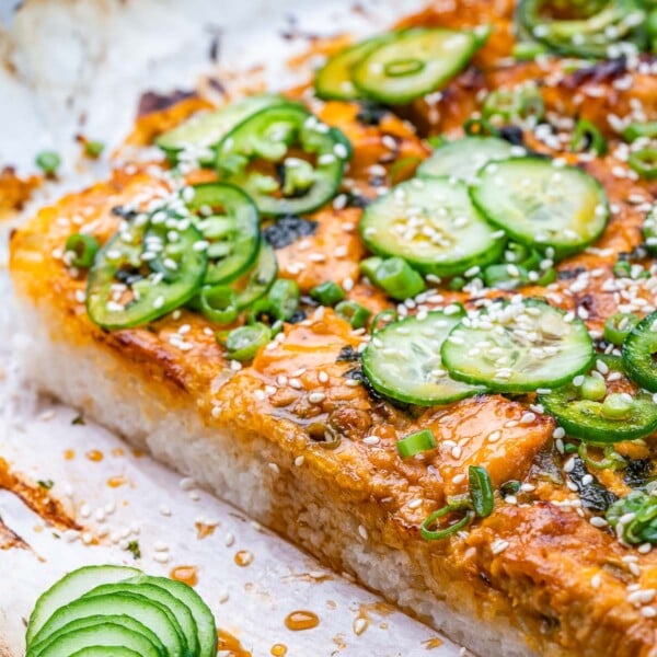side shot of sushi bake on a flat surface topped with sliced cucumber and jalapeno