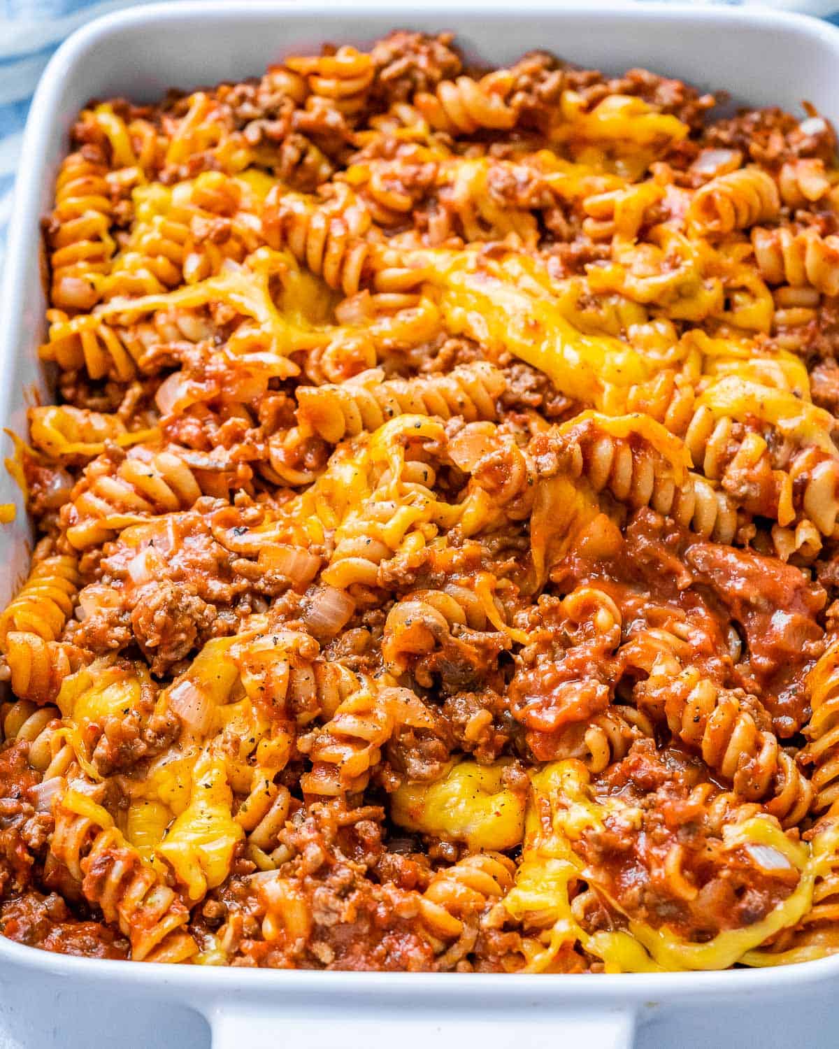 pasta in a meaty red sauce topped with melted cheese in a white casserole dish.