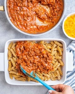 Adding sauce over pasta in a casserole dish.