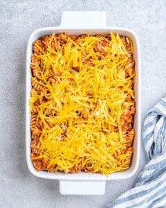 Shredded cheese over a pasta casserole in a white baking dish.