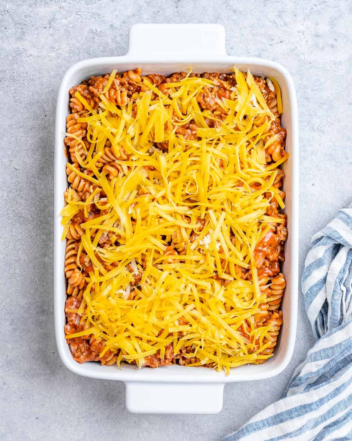 Shredded cheese over a pasta casserole in a white baking dish.