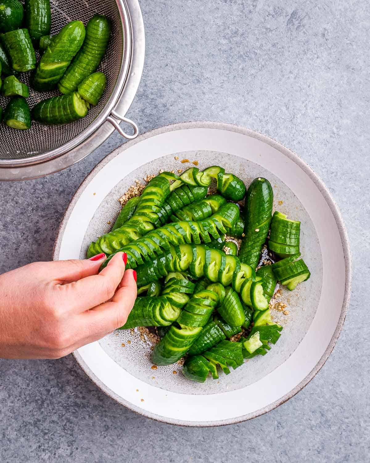 Combining the cucumbers with the dressing in a white bowl.