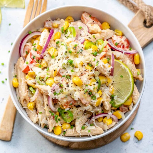 Mexican-style pasta salad in a round bowl, topped with shredded cheese and lime wedges.