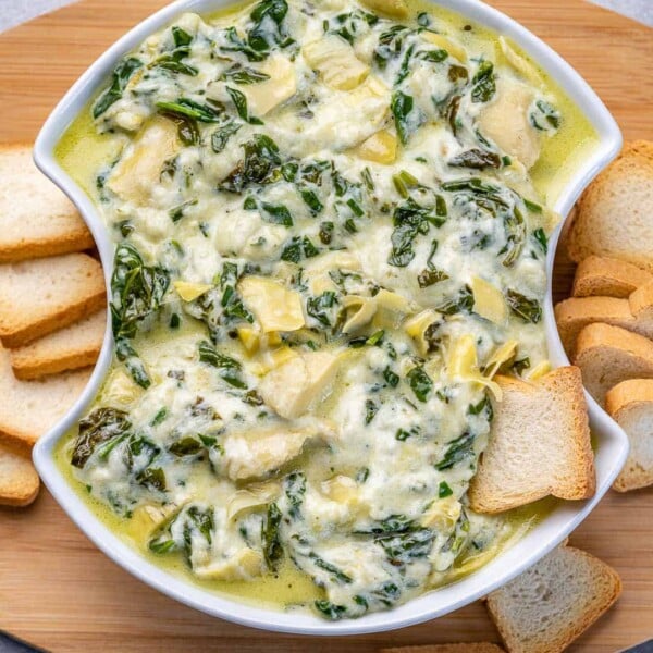 top view of spinach dip in a white bowl with slices of bread on the side.