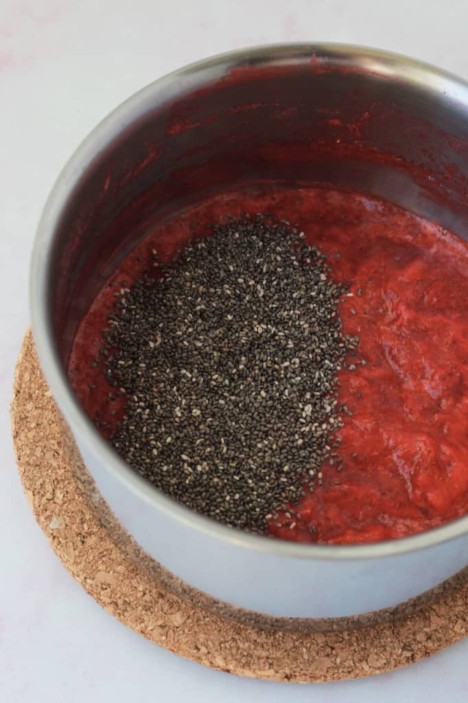 chia seeds added over mashed strawberries in a pot 