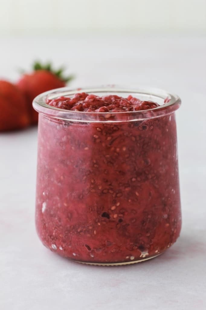 side shot of a jar of strawberry jam filled to the top and is red in color