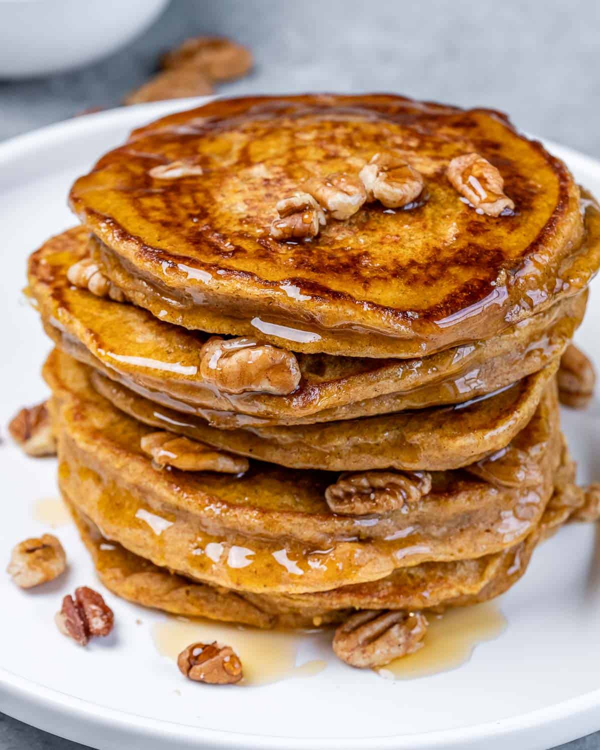 Closeup view of a stack of sweet potato pancakes topped with maple syrup and pecans.