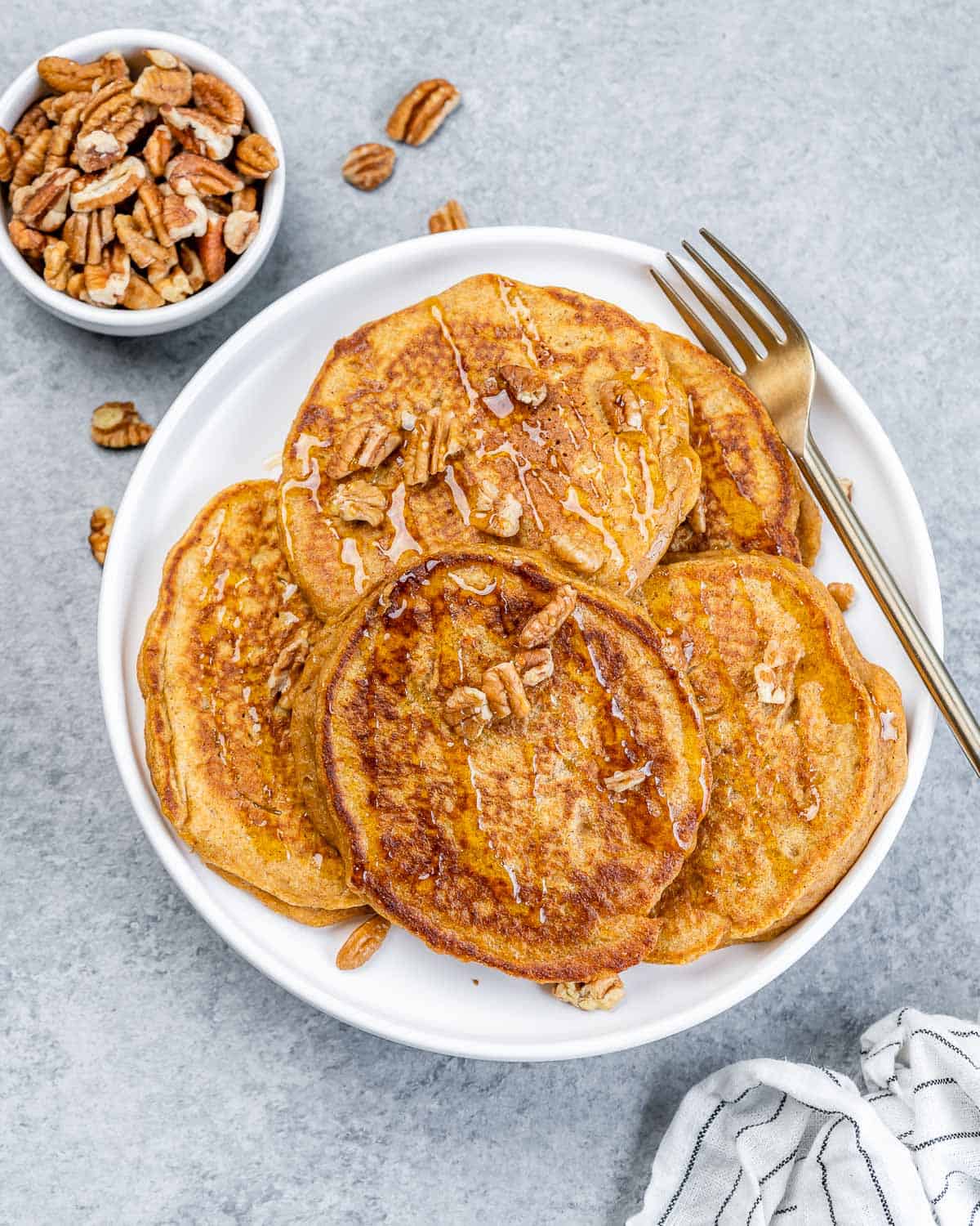 Top view of pancakes on a plate topped with pecans with fork by pancakes.