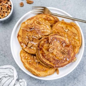 top view of pancakes on a plate topped with pecans with fork by pancakes