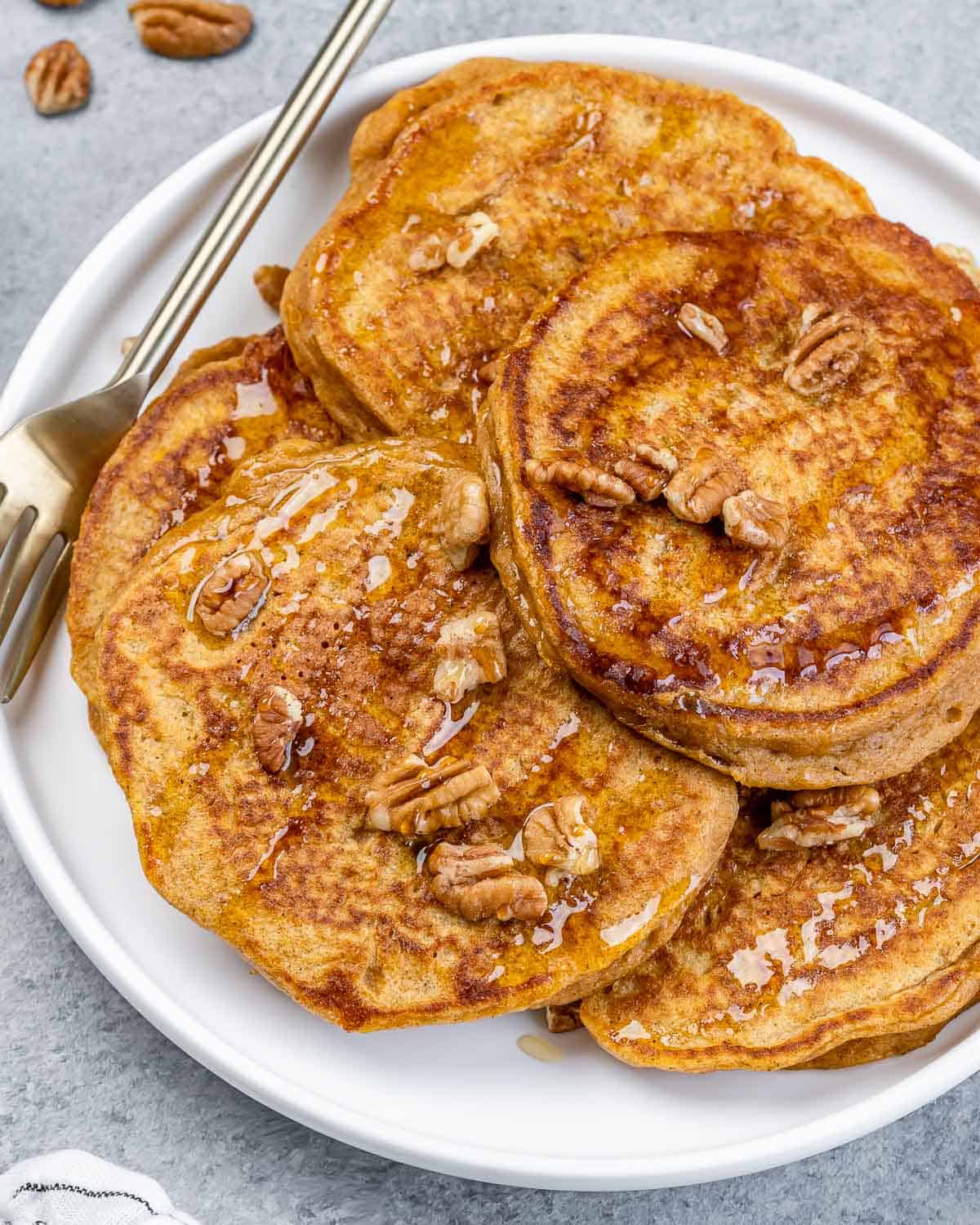 Sweet potato pancakes on a white plate with chopped pecans and a fork.