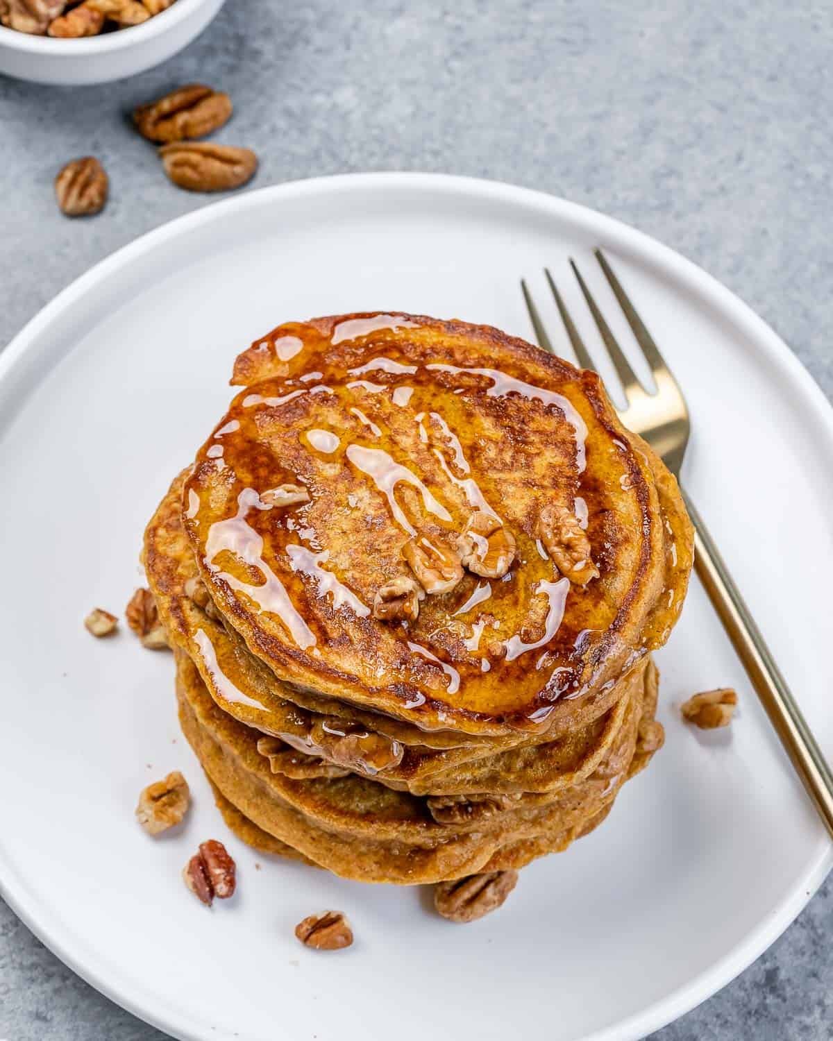Top view of a stack of pancakes drizzled with maple syrup and topped with chopped pecans.