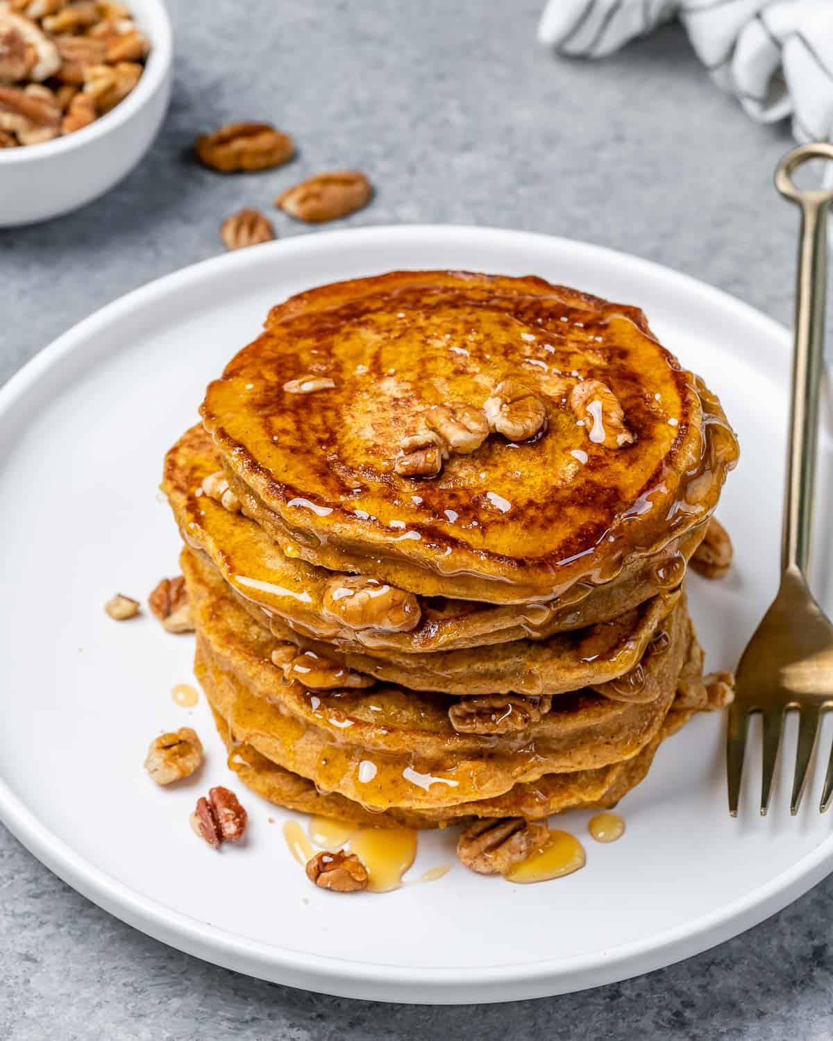 Sweet potato pancakes served in a stack on a white plate with a fork.