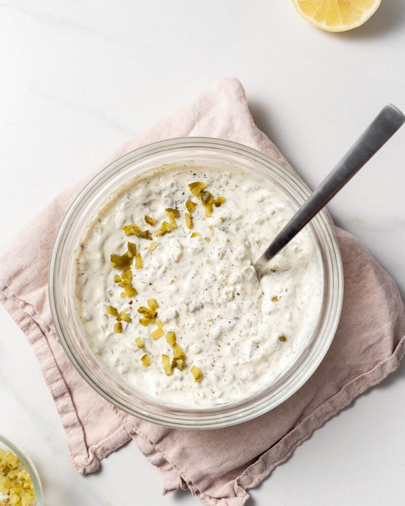 spoon in a bowl of tartar  sauce with dill relish over it 