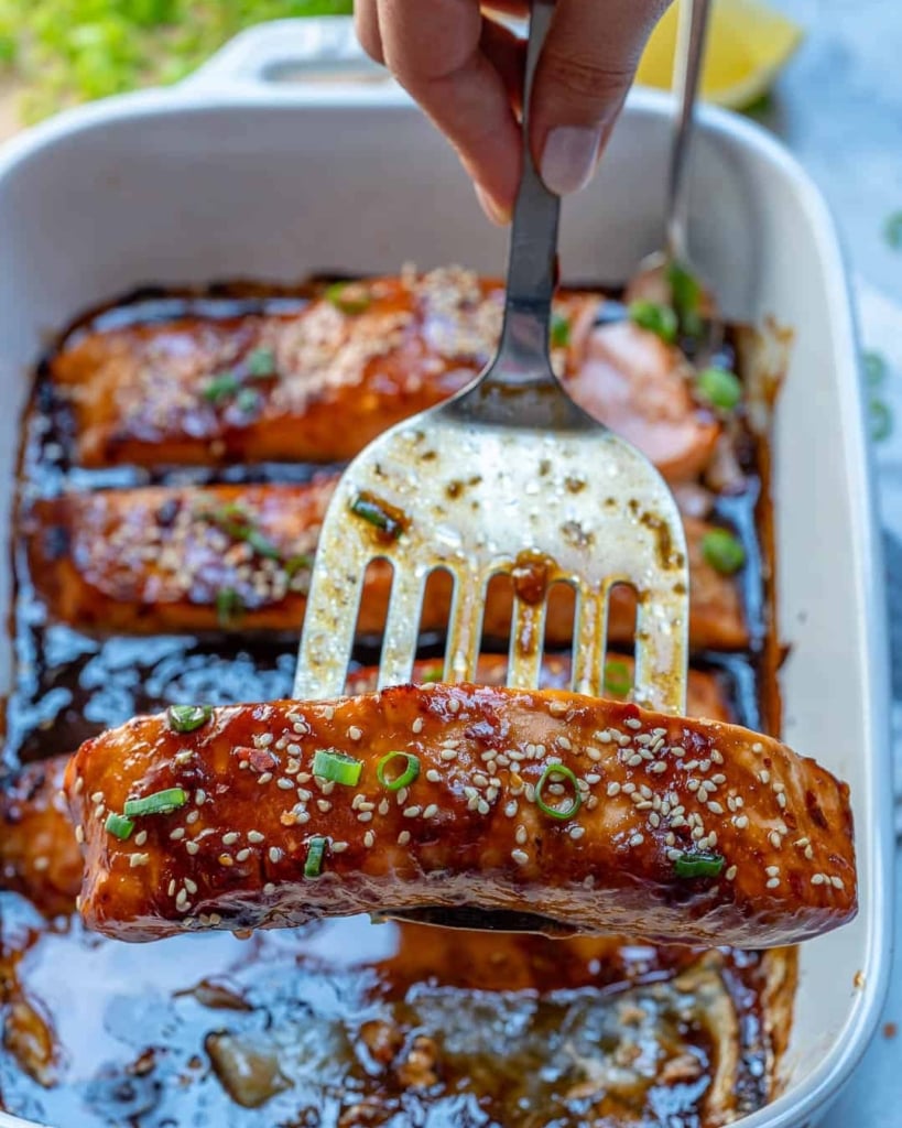 spatula holding a baked teriyaki salmon filet garnished with sesame seeds