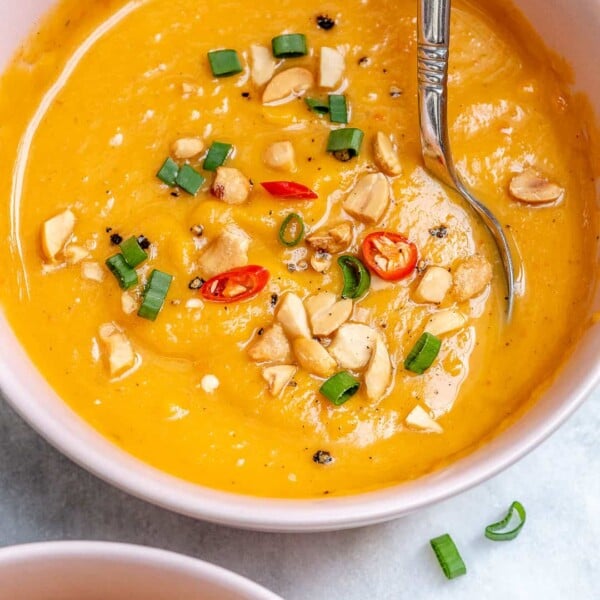 spoon in a bowl of orange colored blended sweet potato and carrot soup in a white bowl.