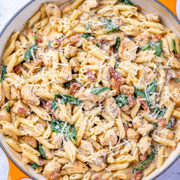 top view chicken pasta with spinach in an orange skillet