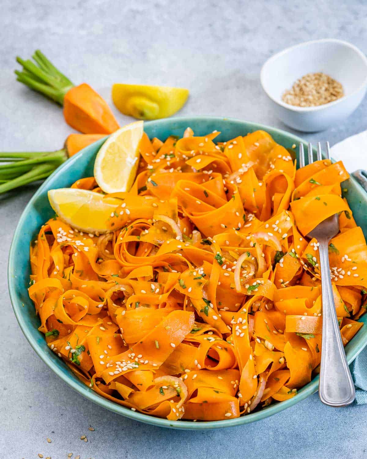 Shredded carrot salad served in a blue bowl with a lemon wedge.