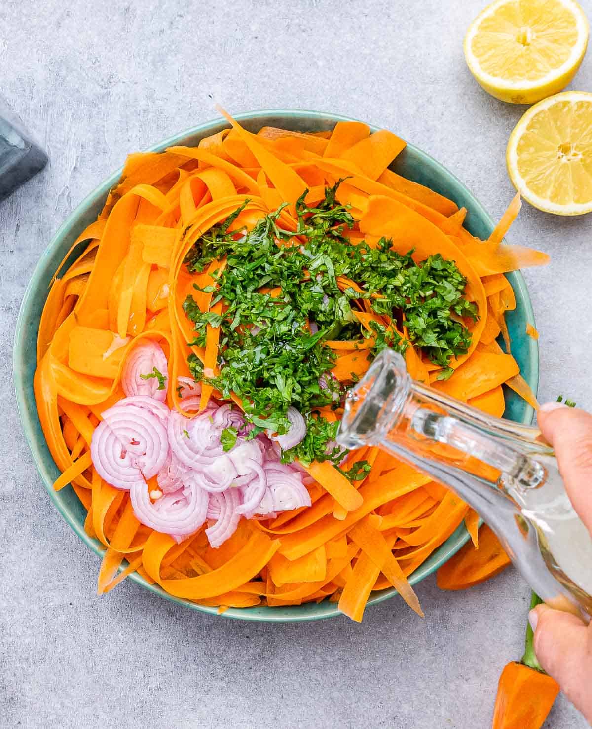 Adding shallots, cilantro and dressing over carrot salad.