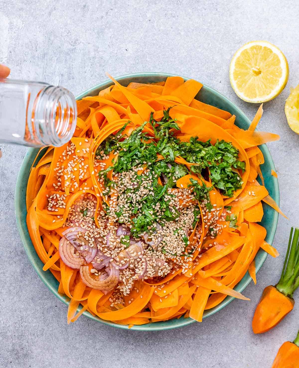Sprinkling sesame seeds over a salad with shredded carrots, cilantro and shallots.