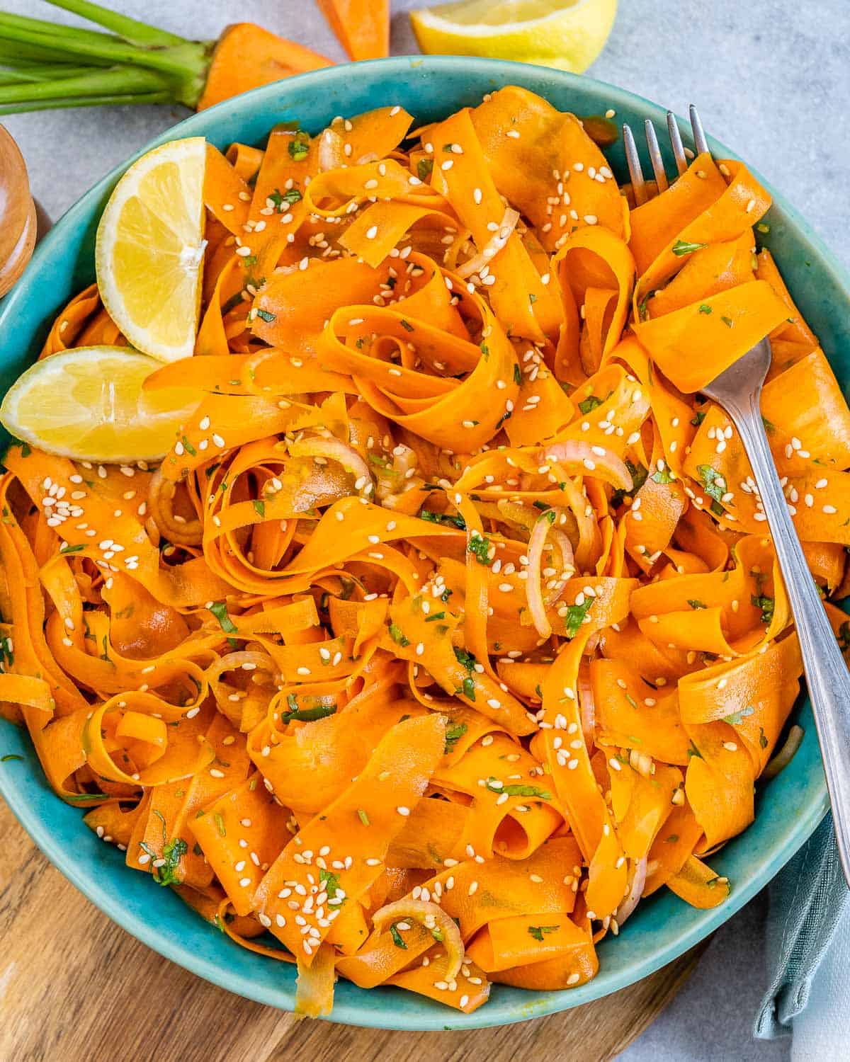 a round blue plate with sliced carrot salad and lemon wedges on the left side of the salad.
